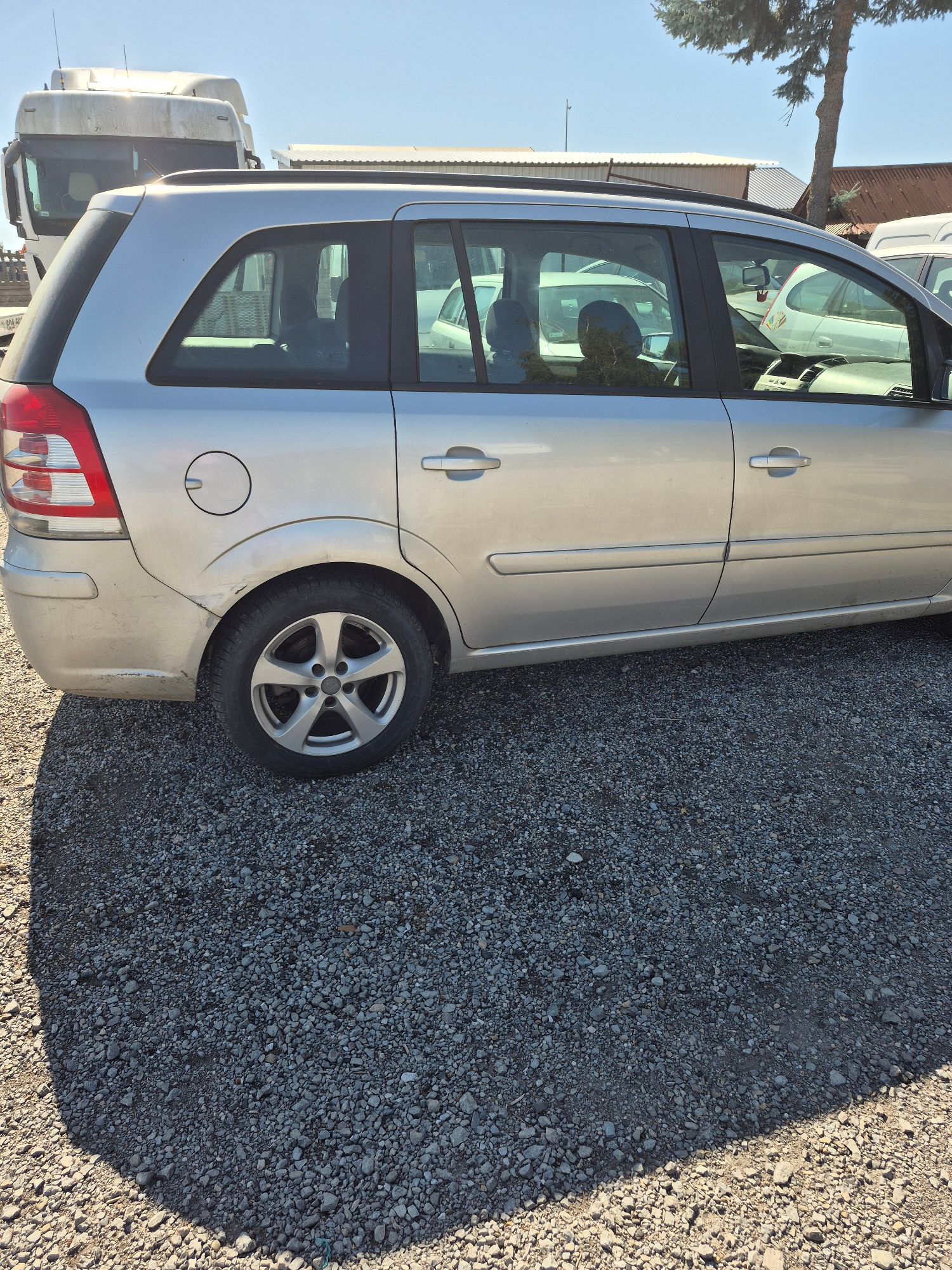 Srebrny Opel Zafira widok z prawej strony pojazdu, widoczne zarysowania w okolicach tylnego koła