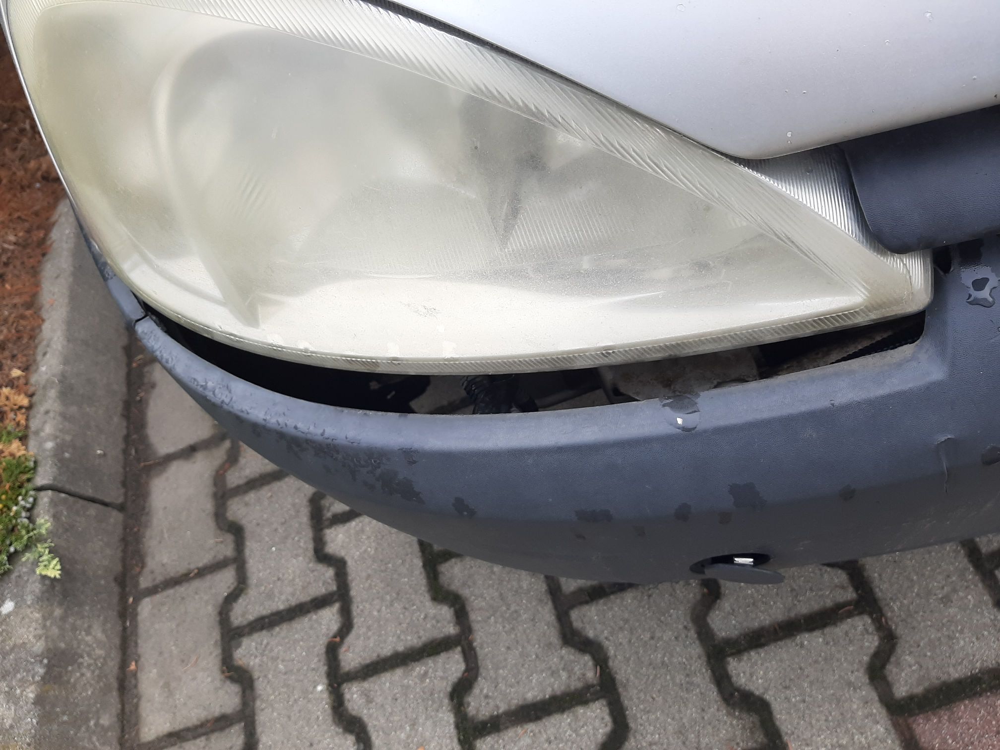 Przedni zderzak samochodowy poluzował się i opadł, tworząc wyraźną szczelinę pod reflektorem.