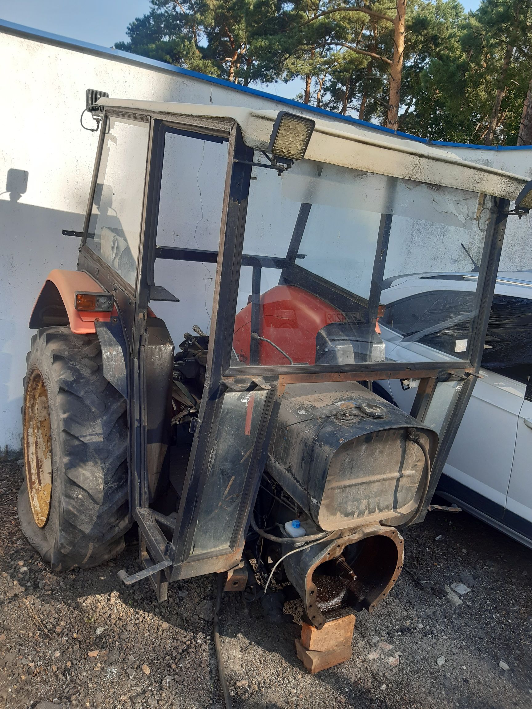 Zdemontowany ciągnik rolniczy z czarną kabiną, dużym tylnym kołem i odsłoniętą obudową sprzęgła.