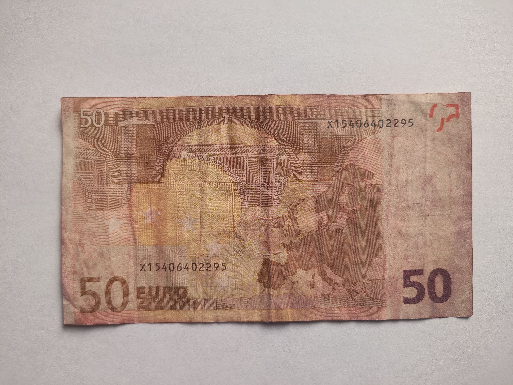 Zużyty i odbarwiony awers banknotu z pierwszej serii z 2002 roku. Widać na nim most, mapę Europy, symbole UE i numer seryjny.