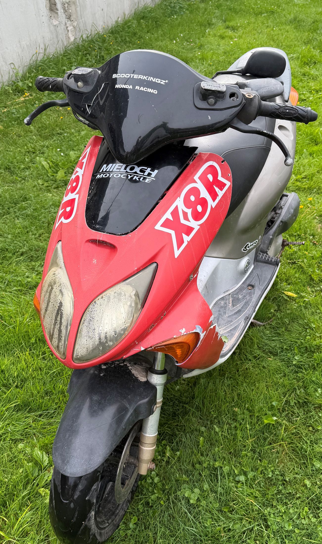 Skuter w kolorze czerwono srebrnym. Widok od przodu motoroweru.