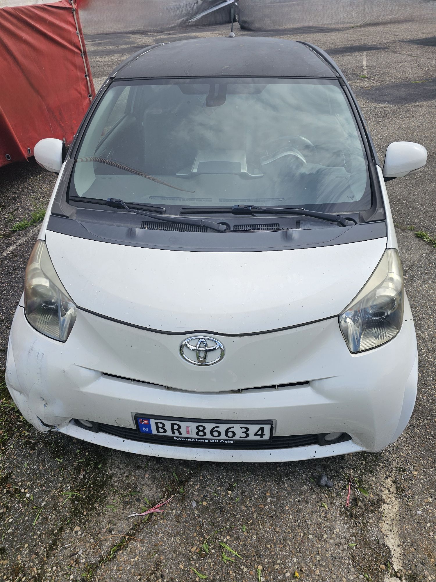 Zdjęcie przedstawia białą Toyotę iQ z norweskimi tablicami rejestracyjnymi z uszkodzonym przednim zderzakiem po prawej stronie