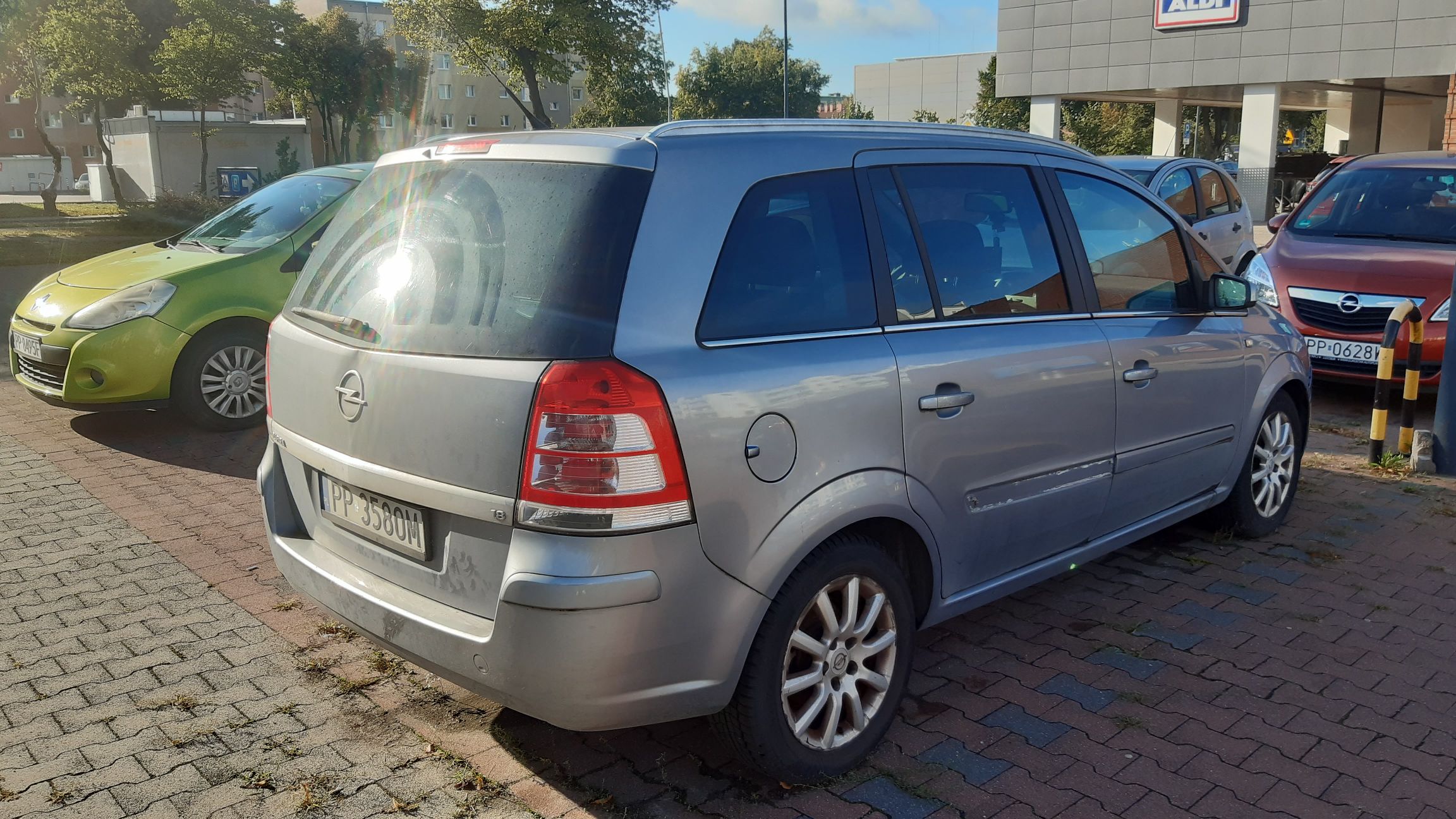 Srebrny samochód osobowy Opel Zafira , sfotografowany z przodu i z lewej strony