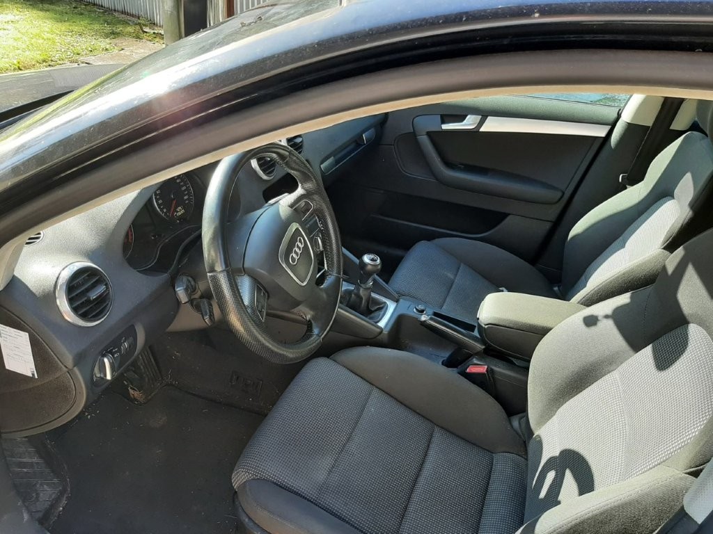 Wnętrze czarnego Audi A3 z ciemną, materiałową tapicerką, czteroramienną kierownicą z logo marki oraz manualną skrzynią biegów.
