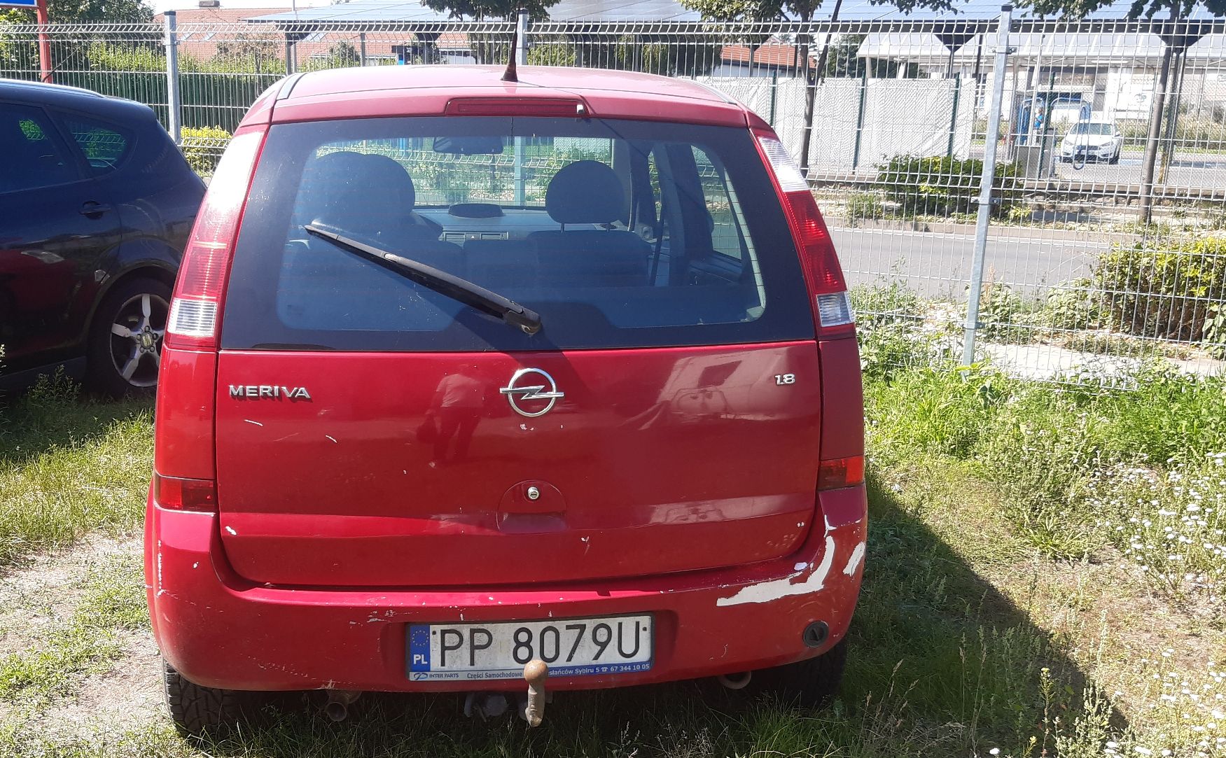 Tył czerwonego minivana z uszkodzeniami lakieru na klapie bagażnika i tylnym zderzaku