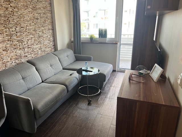 Nowoczesny salon z szarym narożnikiem, kamienną ścianą dekoracyjną i oknem balkonowym.