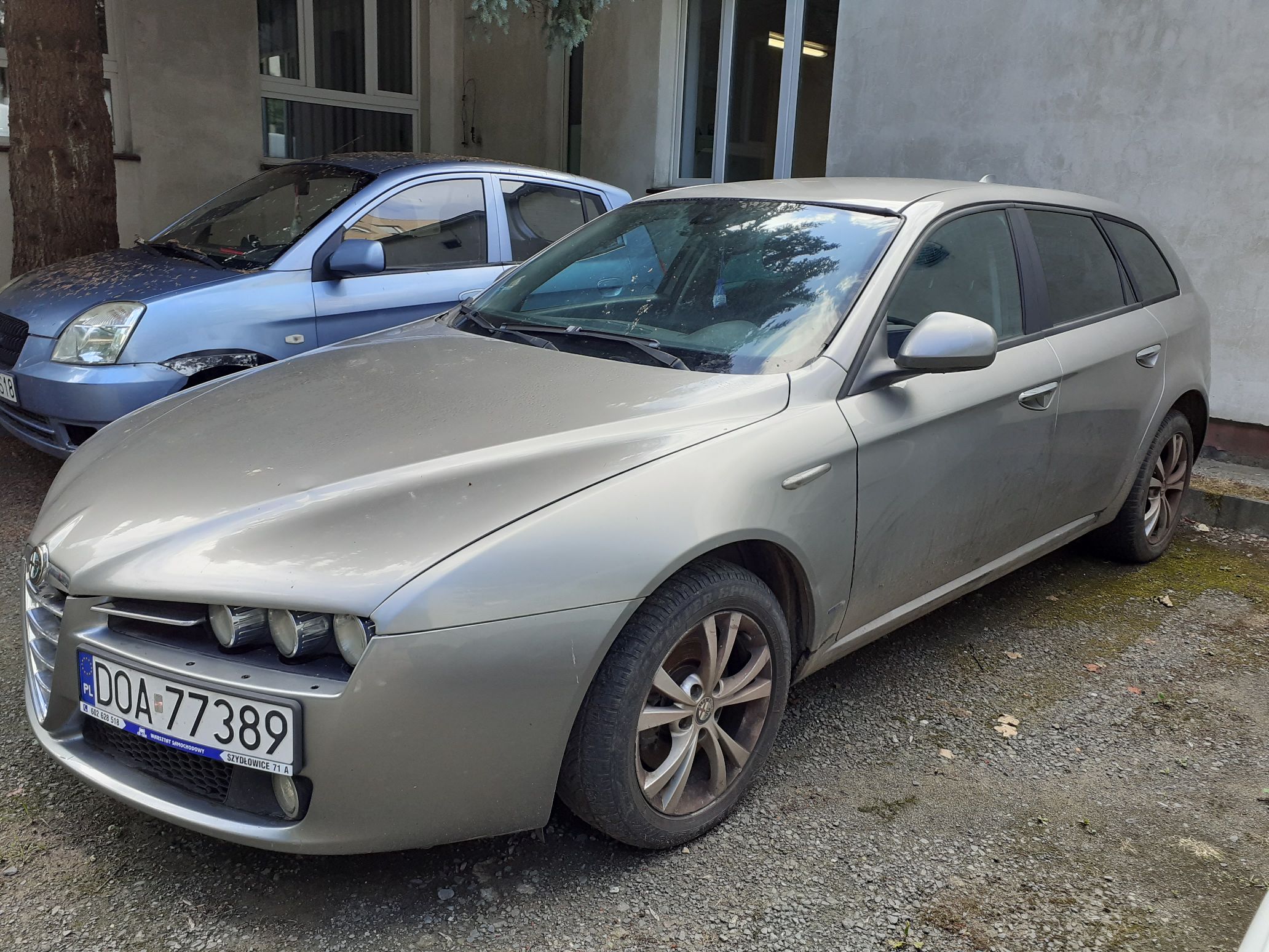 Srebrny samochód osobowy Alfa Romeo 159, przód z potrójnymi, okrągłymi reflektorami oraz grillem w kształcie tarczy
