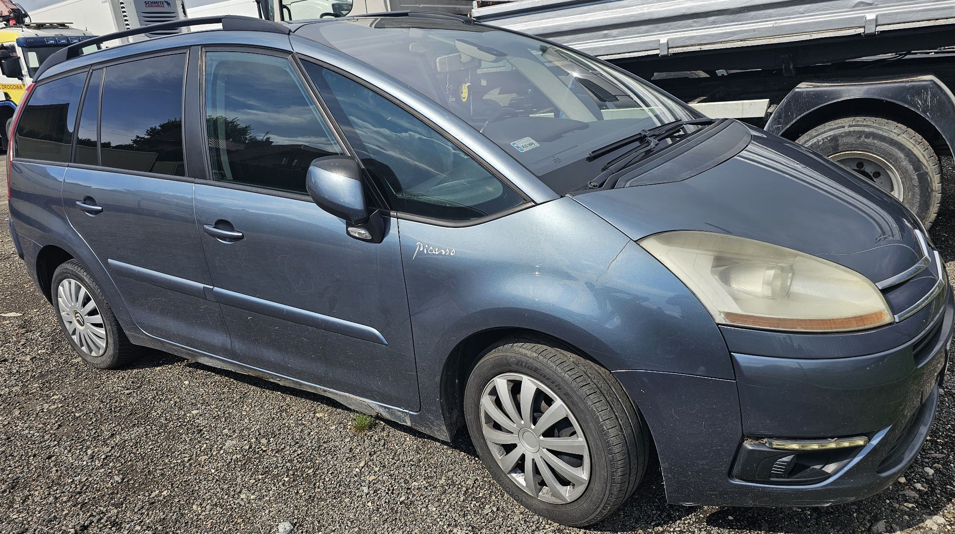 Zdjęcie przedstawia niebieski samochód osobowy Citroën C4 Picasso z dużą przednią szybą i relingami dachowymi.