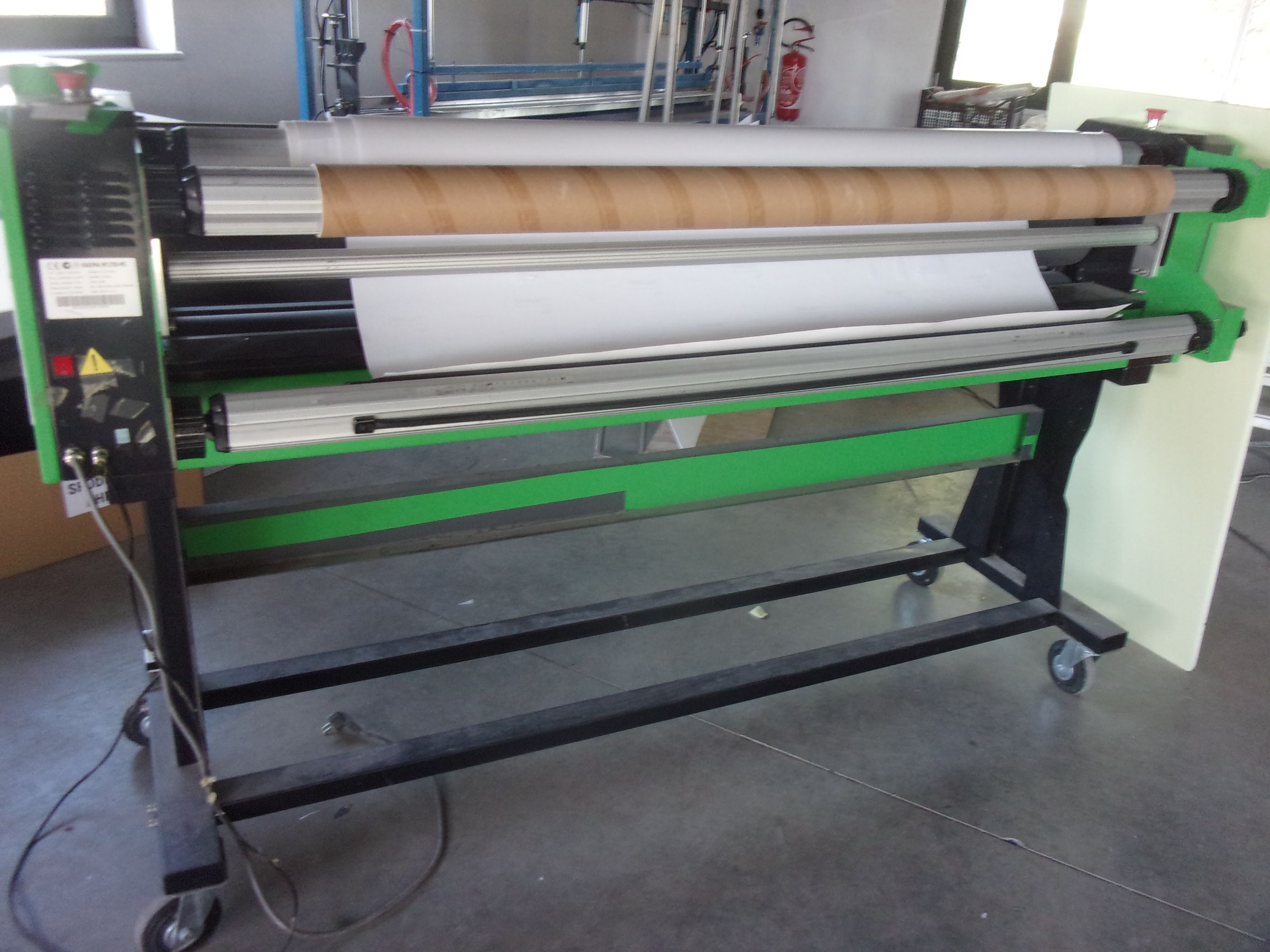 Wielkoformatowy laminator rolowy w kolorze zielono-czarnym, stojący na kołkach w warsztacie lub drukarni.