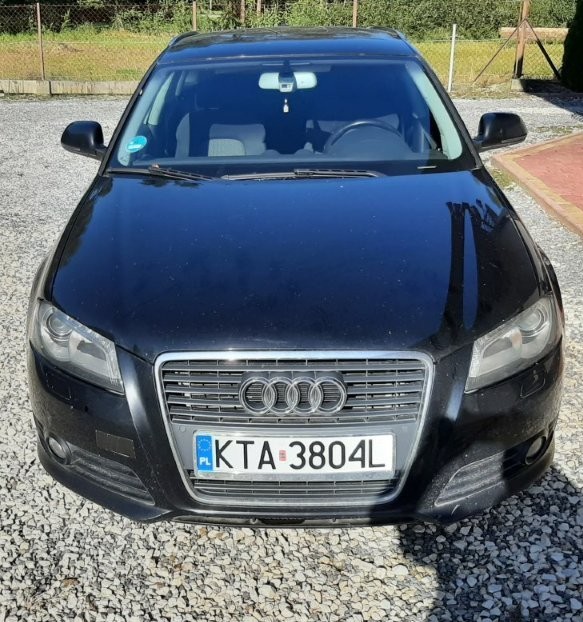 Przód czarnego samochodu osobowego marki Audi A3 z charakterystycznym grillem z logo marki oraz z przednimi reflektorami.