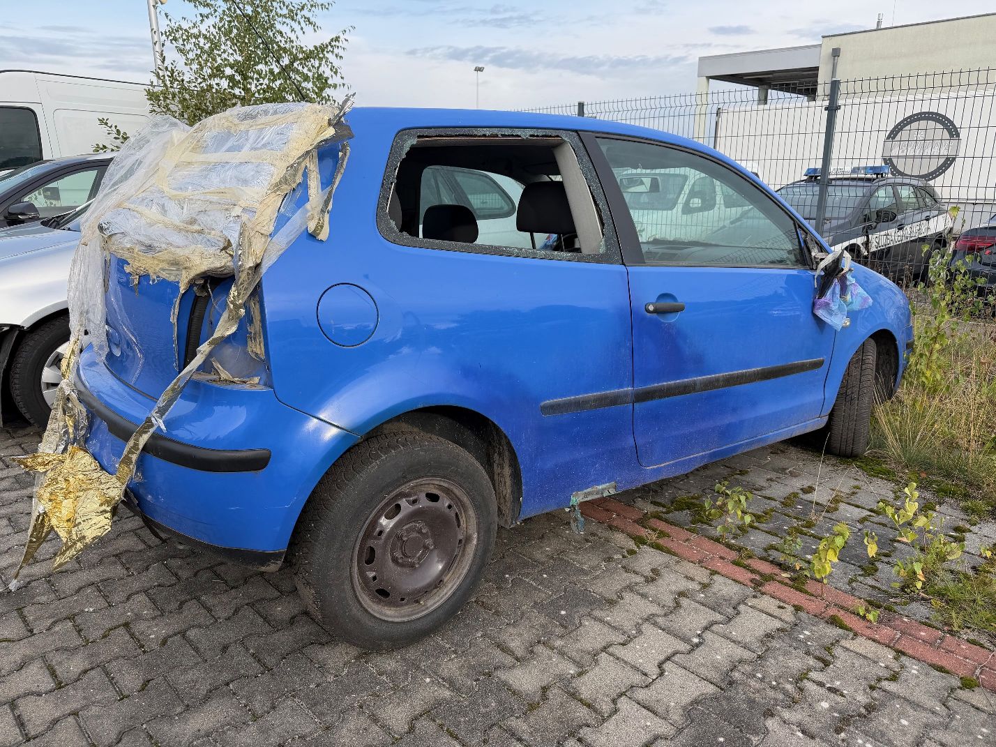 Niebieski Volkswagen Polo, widok z tyłu prawego boku, wybita boczna i tylna szyba, brak tylnej prawej lampy.