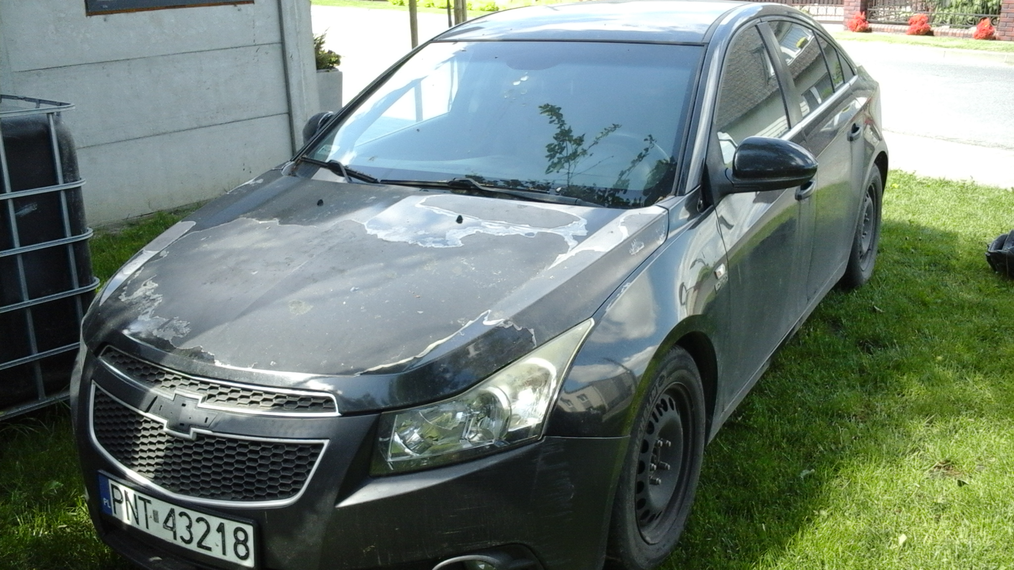 Samochód osobowy Chevrolet Cruze, na masce samochodu widoczne są wyraźne, rozległe łuszczenia i odpryski lakieru bezbarwnego.