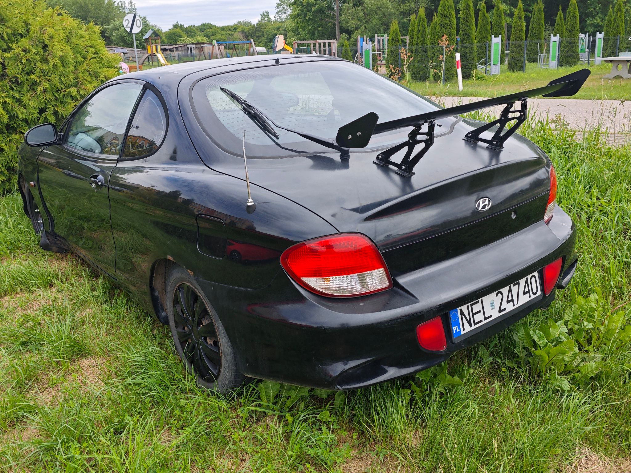 Czarny dwudrzwiowy Hyundai Coupe, na klapie bagażnika zamontowane jest duże sportowe skrzydło.
