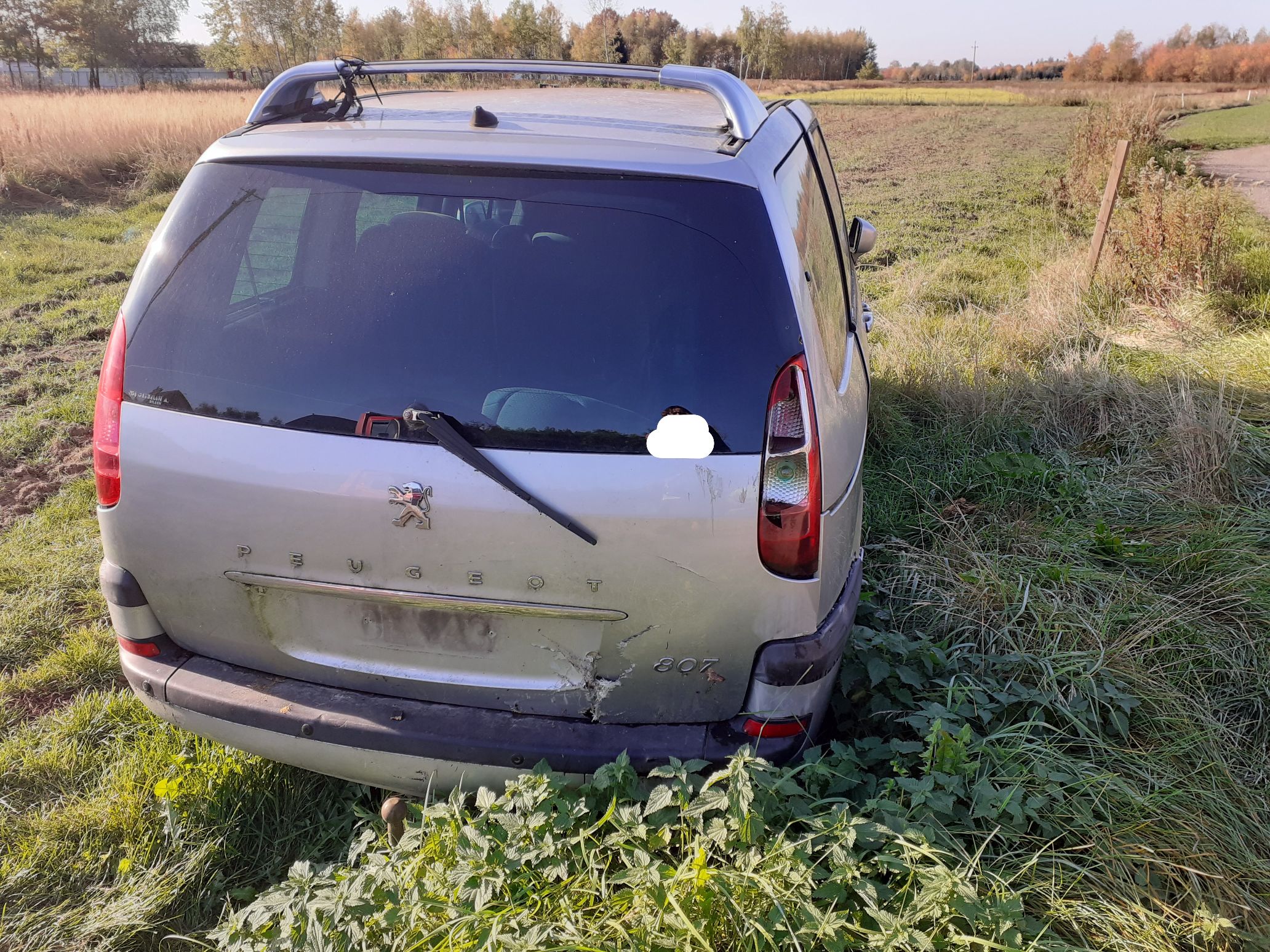 Srebrny samochód osobowy Peugeot typu minivan widoczny z tyłu z widocznymi uszkodzeniami klapy bagażnika i rozbitą lampą.