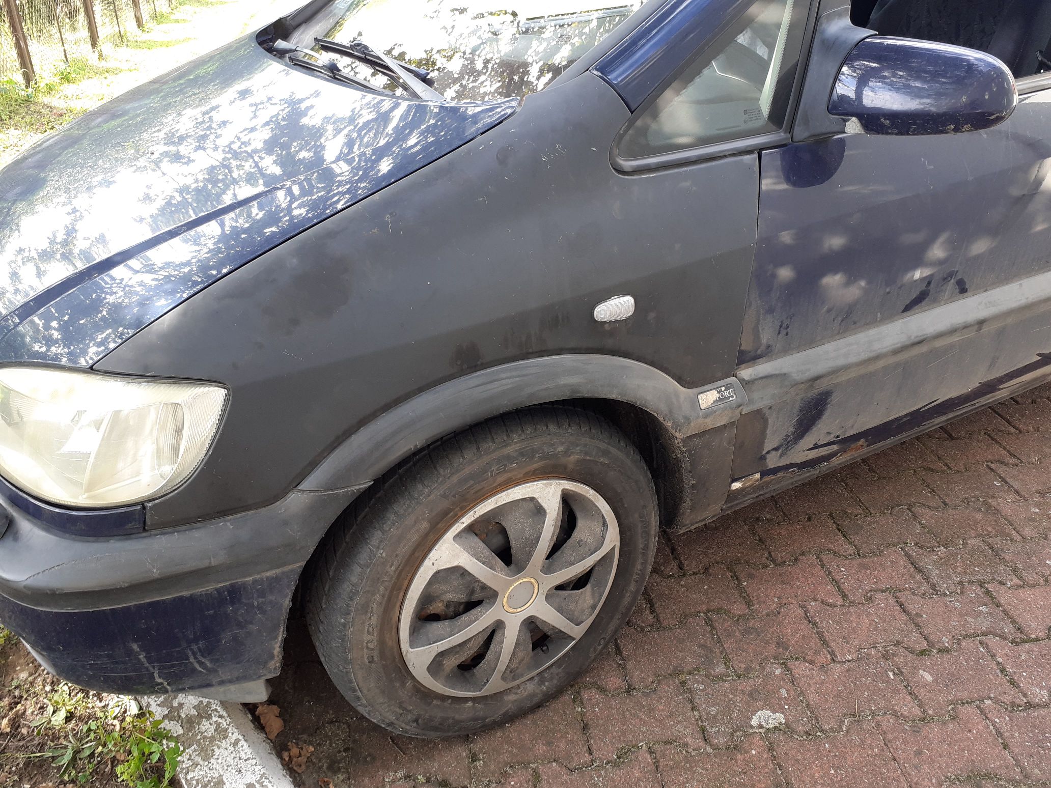 Lewe nadkole koloru czarnego samochodu marki Opel Zafira koloru granatowego.