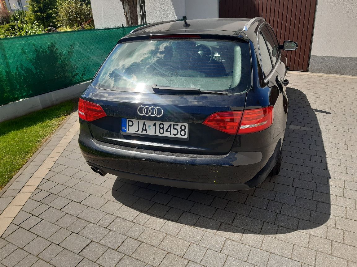 Tył czarnego Audi A4 kombi. Widoczna szyba z wycieraczką, klapa bagażnika z logo, lampy i tablica rejestracyjna.