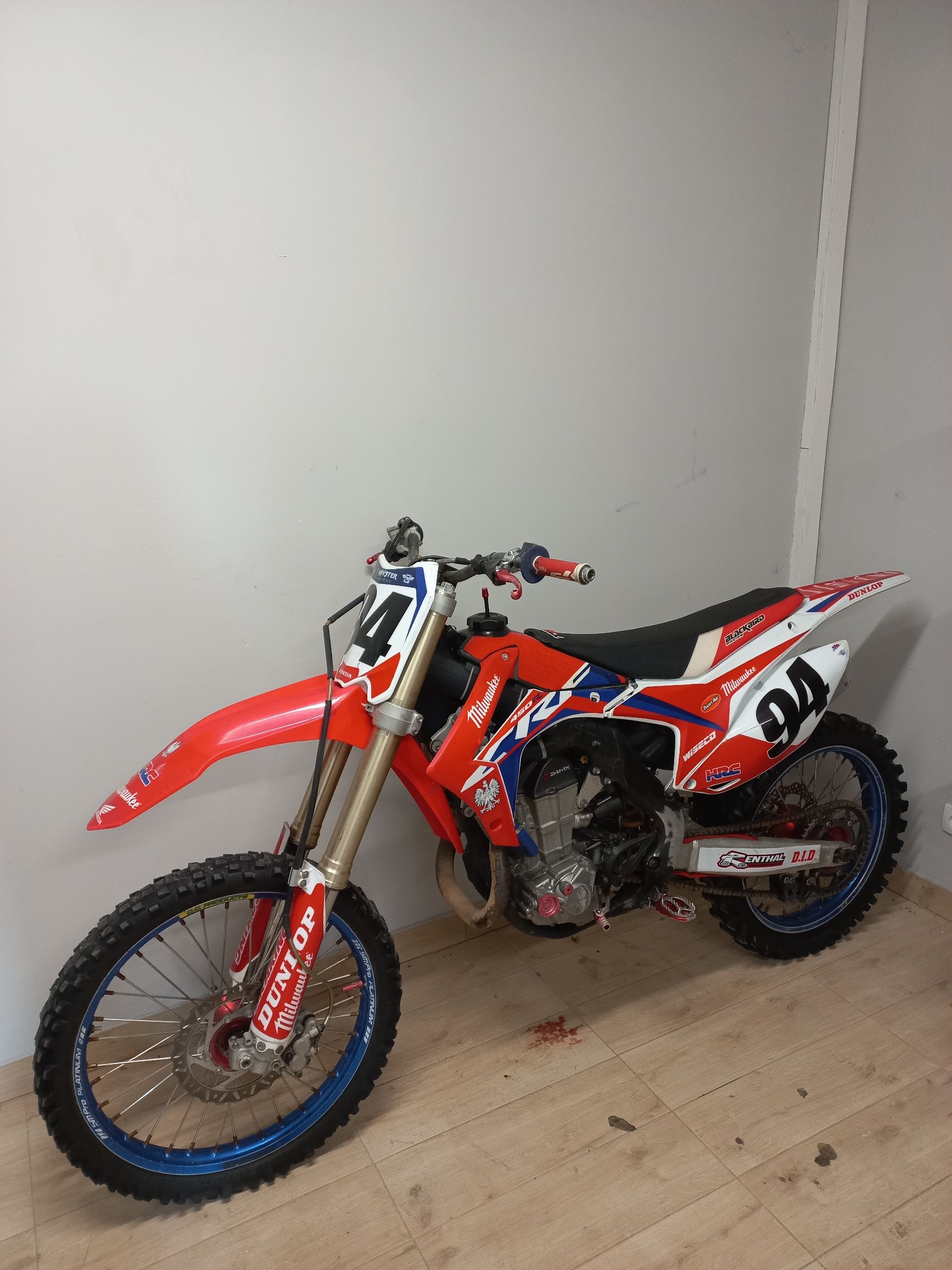 Czerwono-biały motocykl crossowy Honda CRF z numerem startowym 94, zaparkowany bokiem w jasnym pomieszczeniu