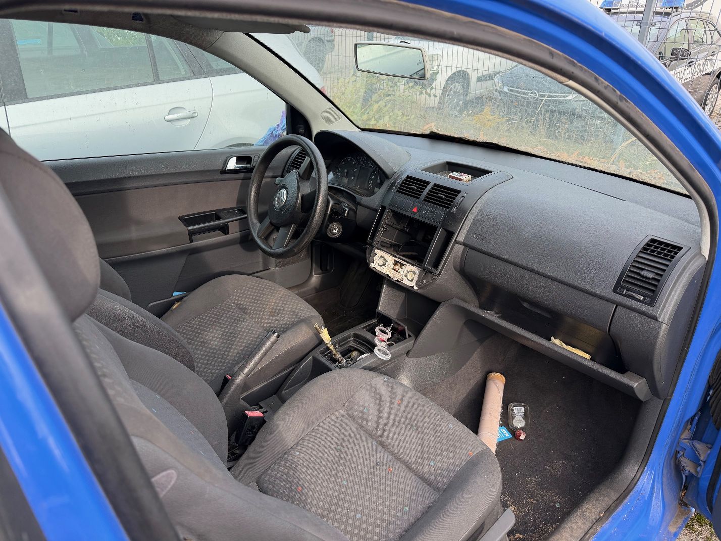 Niebieski Volkswagen Polo, wnętrze samochodu wyraźnie zabrudzone, tapicerka welurowa w kolorze szarym, brak elementów konsoli.