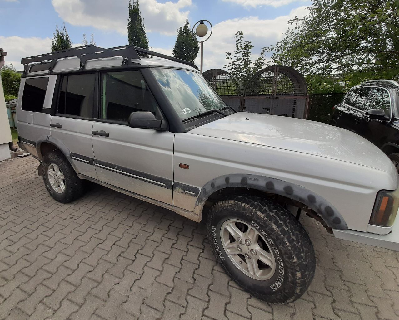 Samochód Land Rover terenowy typu SUV w kolorze srebrnym. Pojazd ma bagażnik dachowy, przyciemniane szyby.