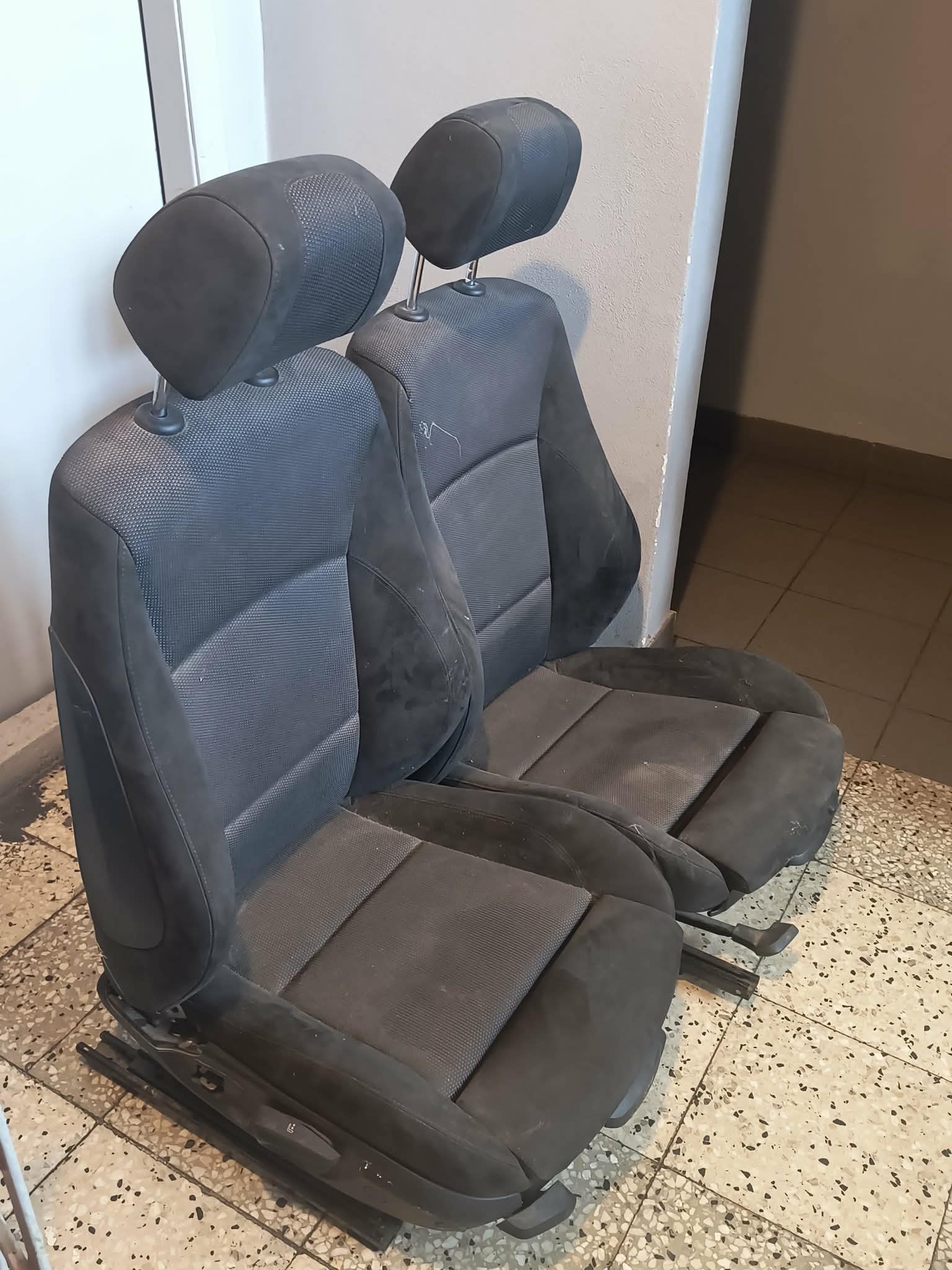 Dwa przednie fotele samochodowe do BMW. Każdy fotel ma regulowany zagłówek na dwóch metalowych prowadnicach