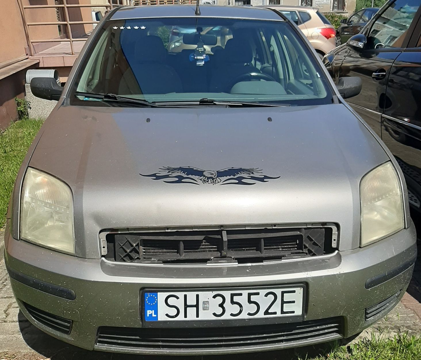 Samochód widoczny z przodu. Brak plastikowej kratki z przodu auta, zmatowiałe reflektory, naklejka z orłem na masce.