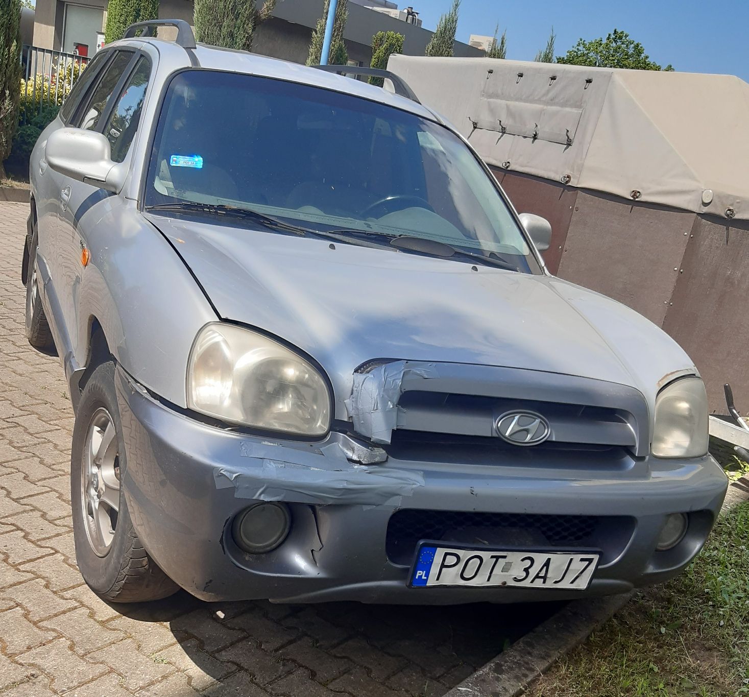 Srebrny samochód osobowy marki Hyundai model Santa Fe pierwszej generacji. Pojazd nosi wyraźne ślady uszkodzeń z przodu.