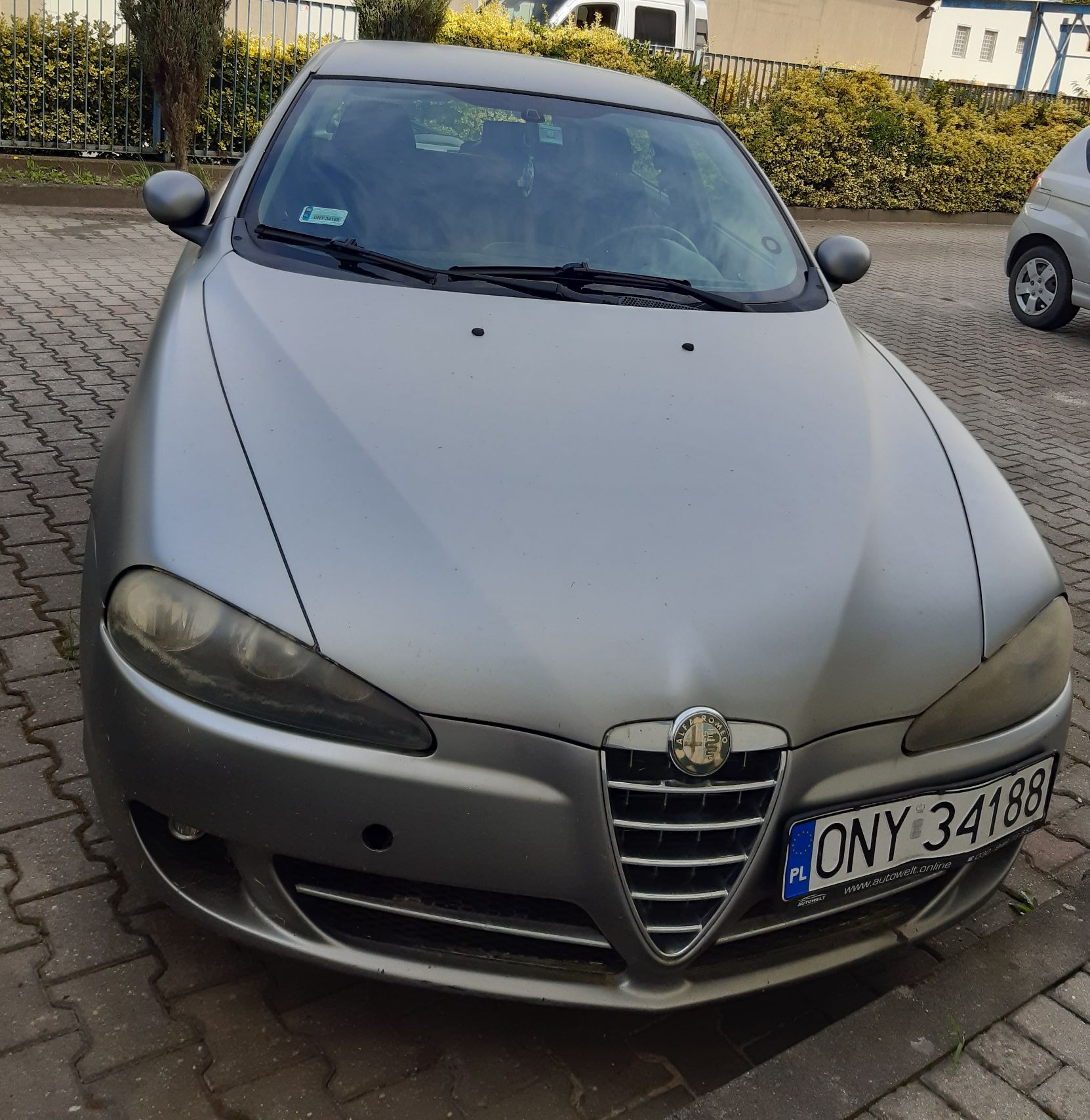 Szare auto osobowe marki Alfa Romeo model 147, z charakterystyczną osłoną chłodnicy w kształcie tarczy z logo producenta.