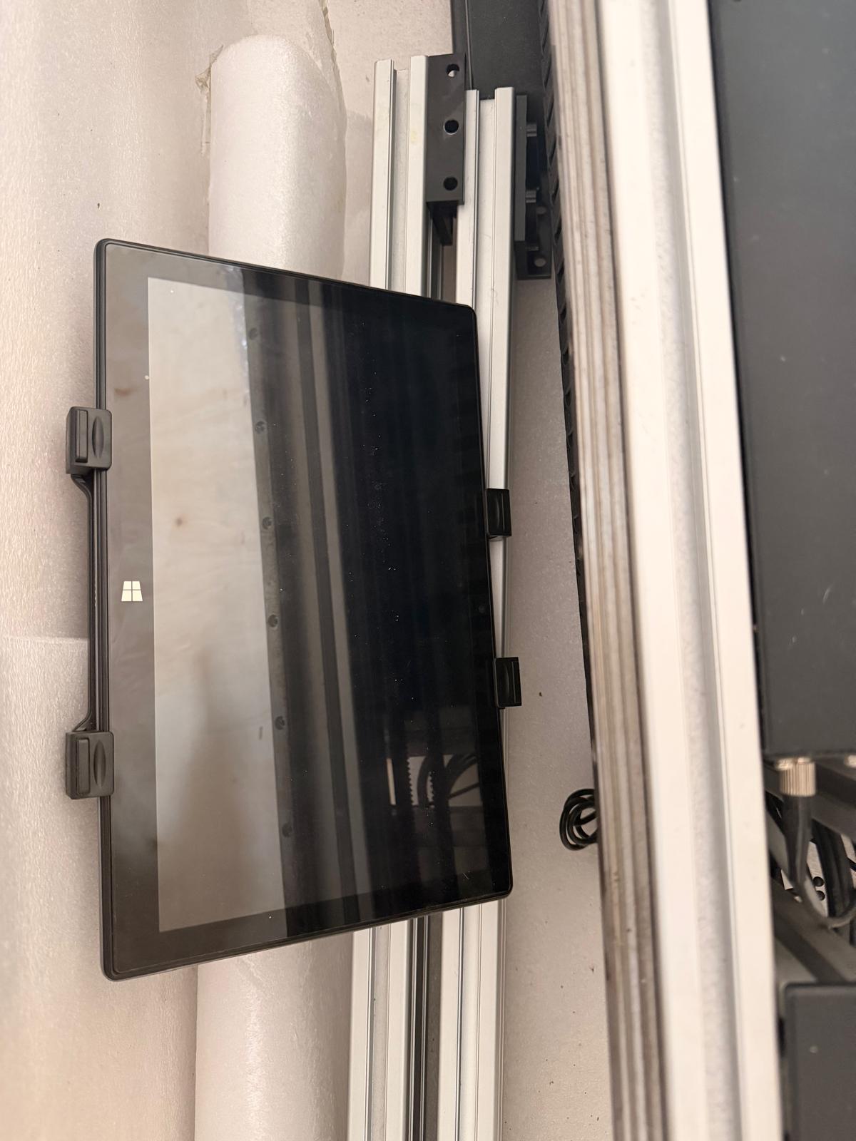 Tablet z logo Windows. Urządzenie znajduje się obok metalowych elementów maszyny.