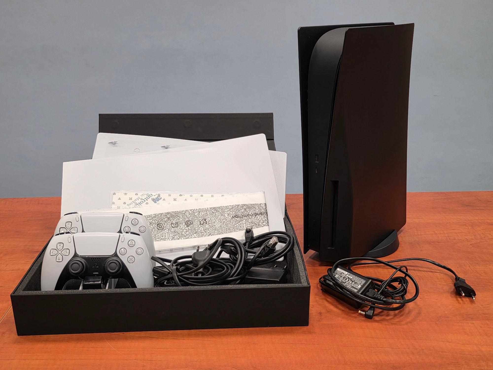 Konsola Sony PlayStation 5 wraz z dwoma bezprzewodowymi kontrolerami koloru szarego, kabel zasilający, HDMI, USB koloru czarnego