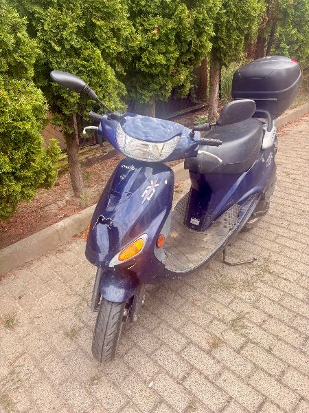 Granatowy motorower z czarnym siedzeniem z tylnym kufrem do przechowywania. Widok z boku.