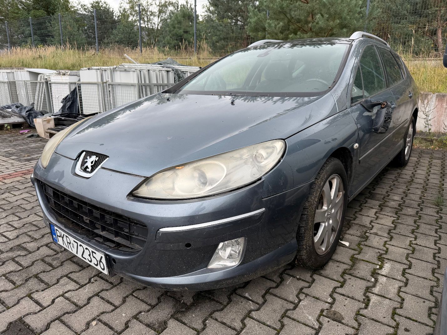 Szary Peugeot 407 SW, widok z przodu lewego boku, srebrne relingi dachowe, zmatowiałe reflektory, uszkodzone lusterko.