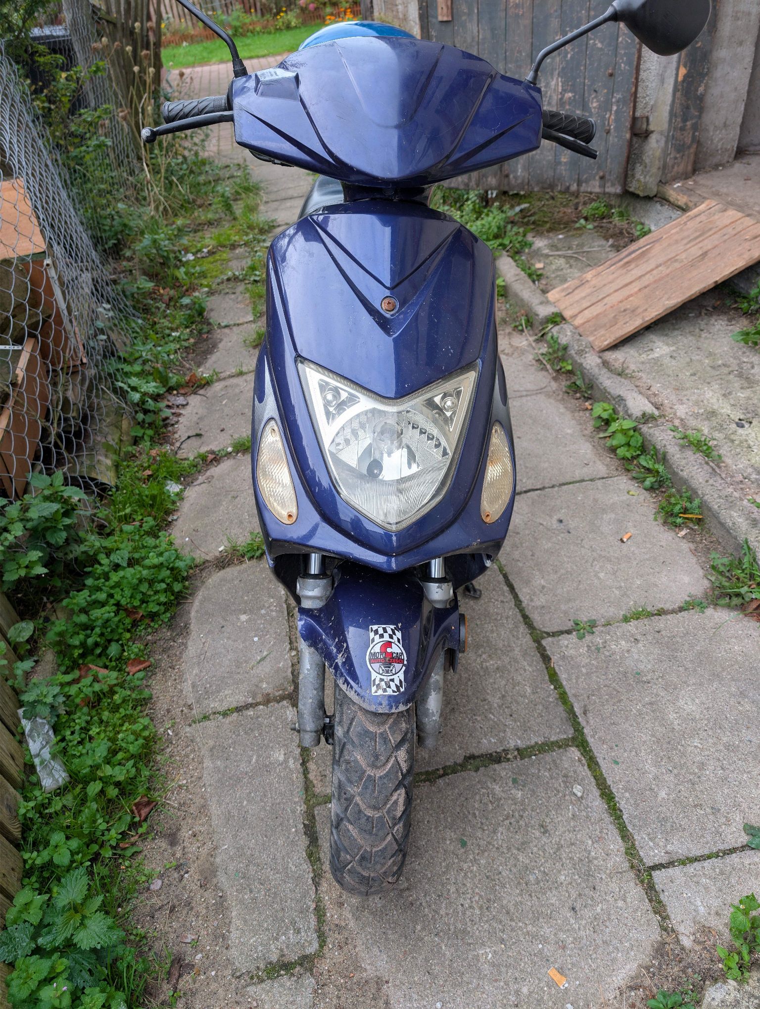 Niebieski motorower sfotografowany z przodu. Ma ciemnoniebieskie plastikowe owiewki, duży przedni reflektor.