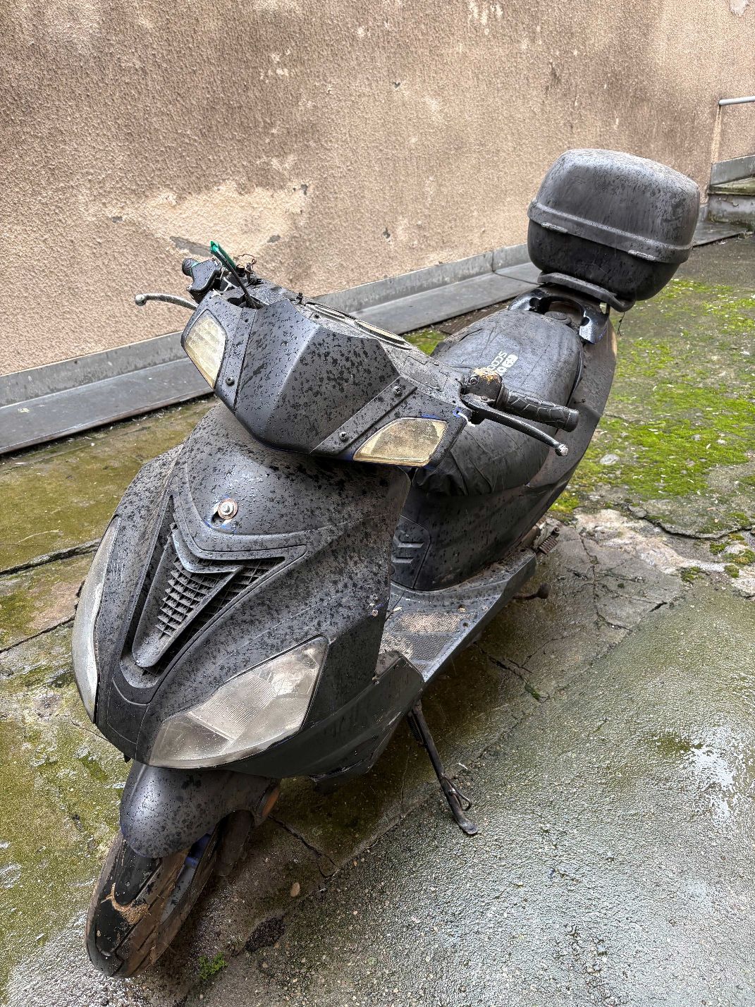 Motorower koloru czarnego wraz z szarym kufrem, widok od frontu.