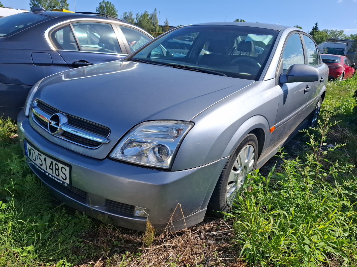 samochód osobowy koloru srebrnego marki OPEL Vectra stojący na zewnętrznym parkingu.