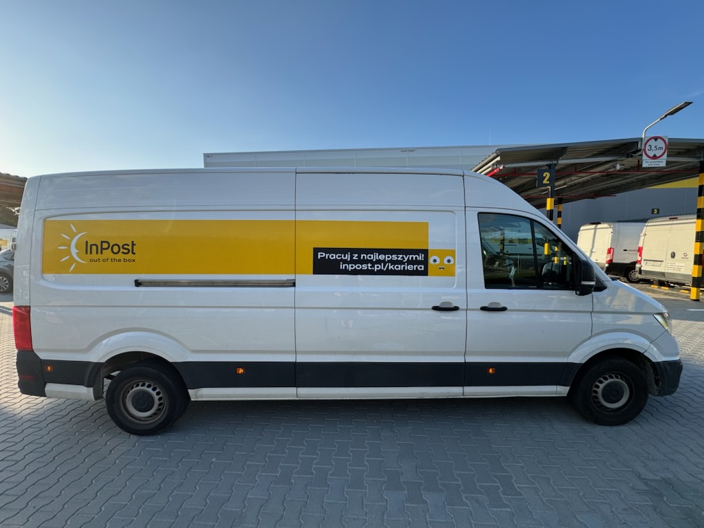 zdjęcie przedstawia prawy bok białego samochodu dostawczego Volkswagen Crafter z wysokim dachem, oklejony w barwy firmy InPost