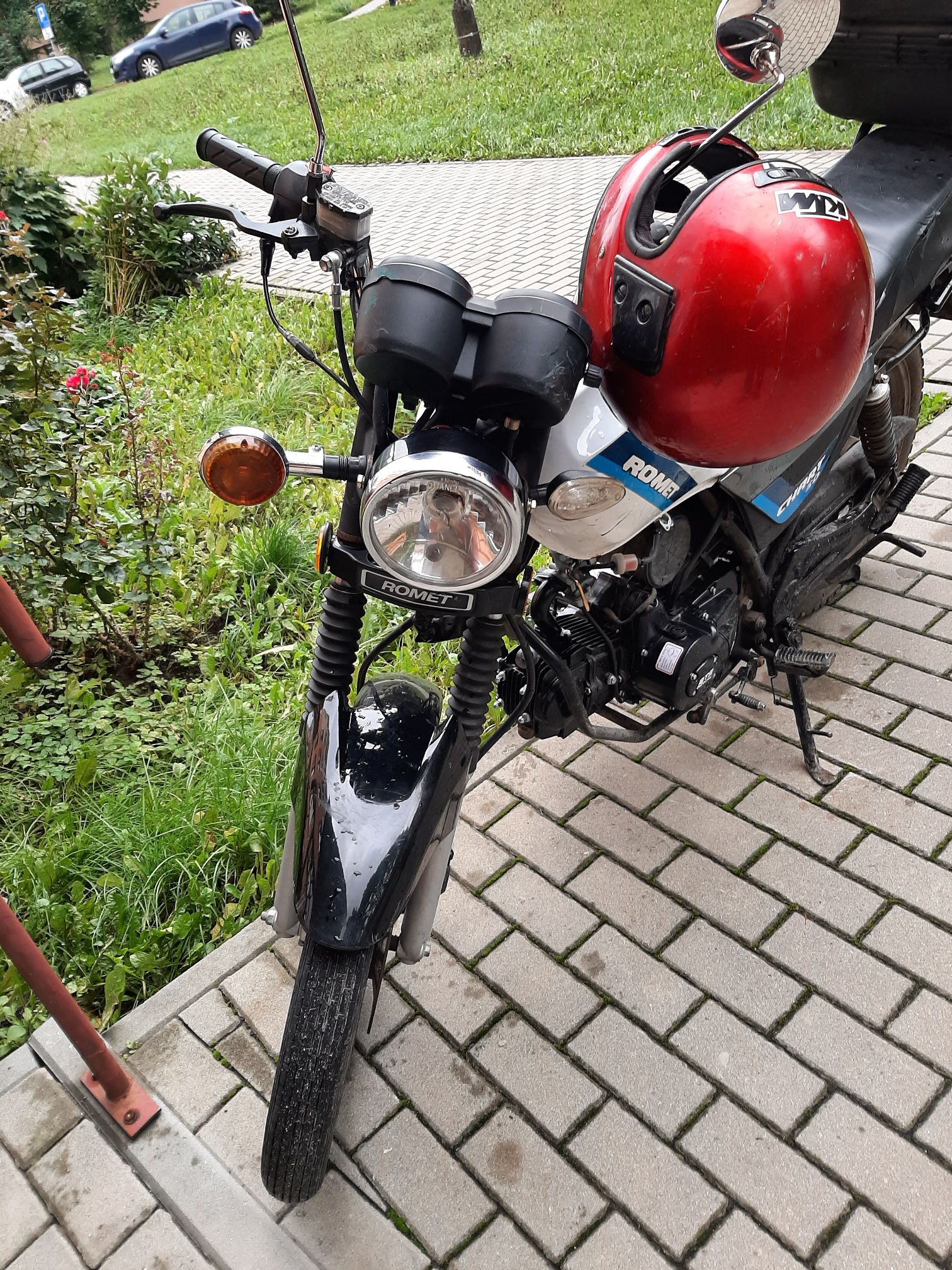 Motorower Romet Chart 50 z okrągłą przednią lampą, dwoma zegarami, czarnym lusterkiem oraz cienkimi kołami ze szprychami.