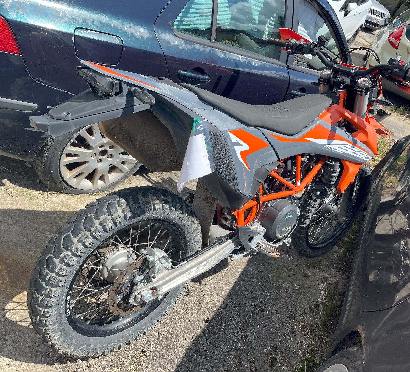 Tył i prawy bok motocykla z pomarańczowo-szarymi elementami nadwozia, grube bieżnikowane opony, metalowa rama i amortyzatory.