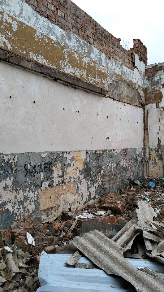 Zniszczone wnętrze starego budynku z popękanymi, łuszczącymi się tynkami. Na ścianach widoczne są graffiti i ślady zużycia