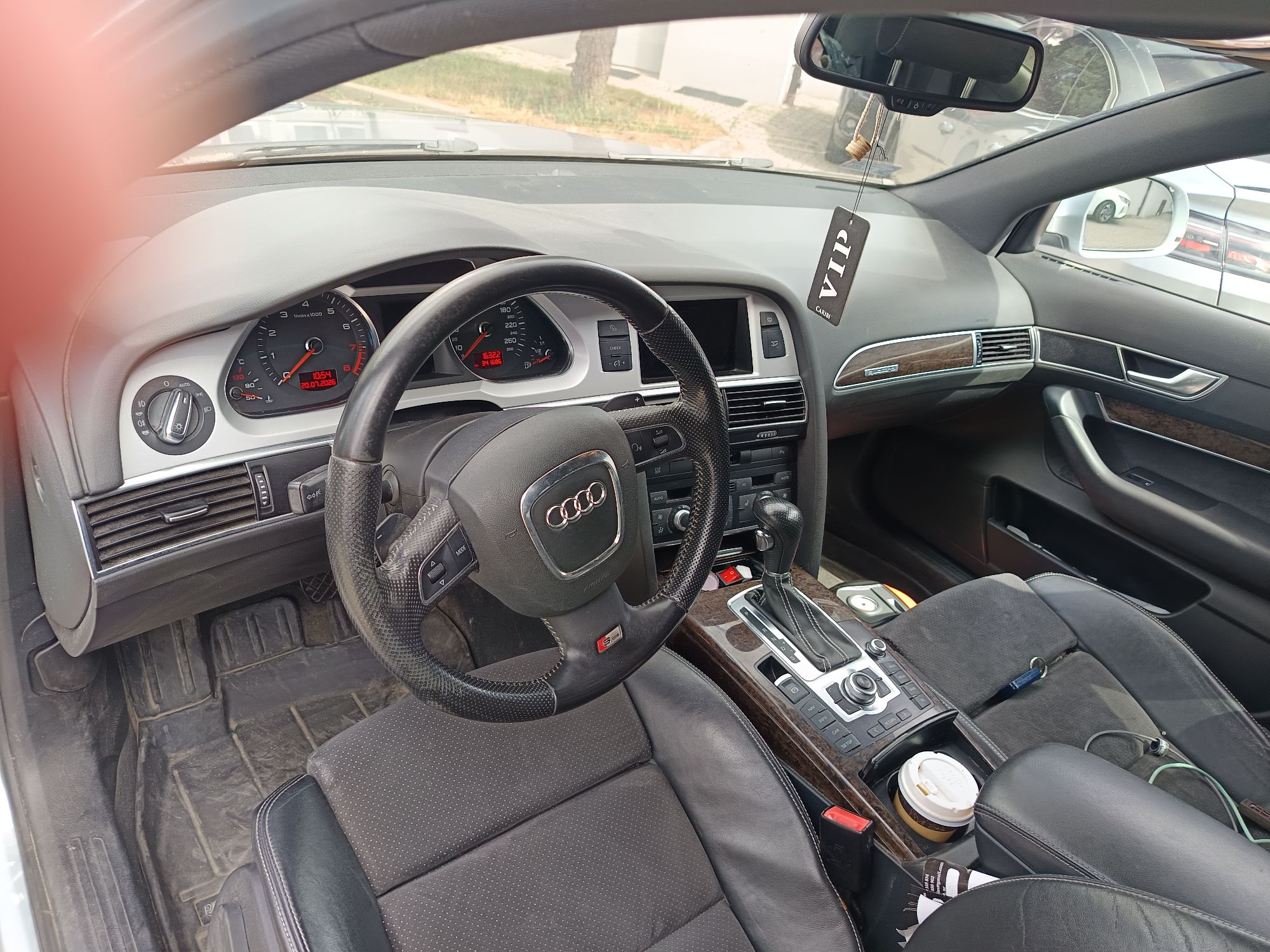 Wnętrze Audi A6: czarna kierownica z logo, deska rozdzielcza, fotele i konsola środkowa z automatyczną skrzynią biegów.