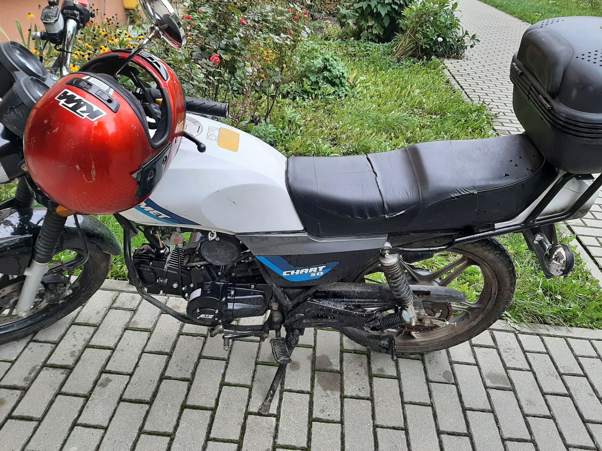 Motorower typu naked w kolorze białym, z czarnym, długim siedzeniem i czarnymi elementami silnika.