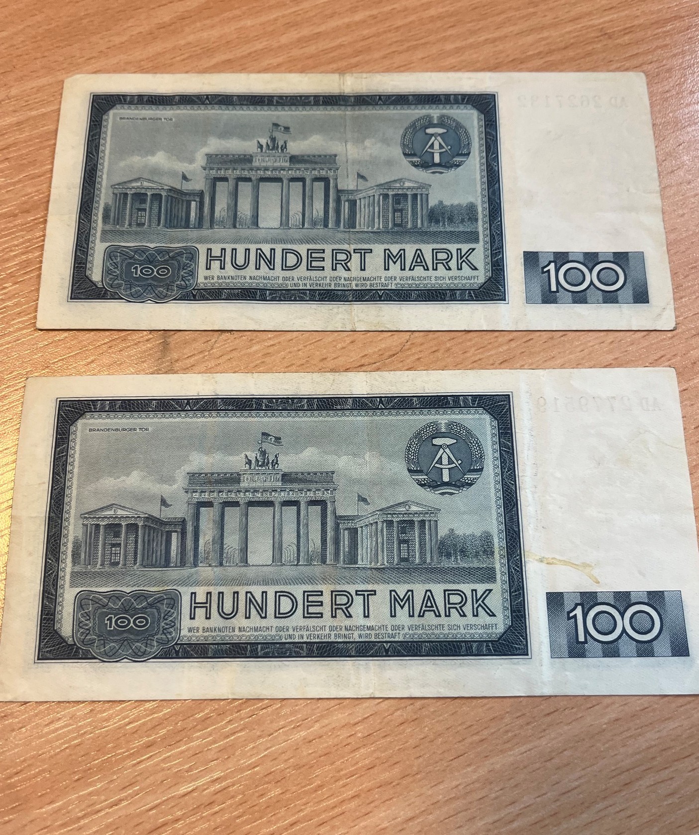 Rewersy dwóch banknotów o nominale 100 marek NRD z emisji z 1964 roku, ułożone pionowo jeden pod drugim.