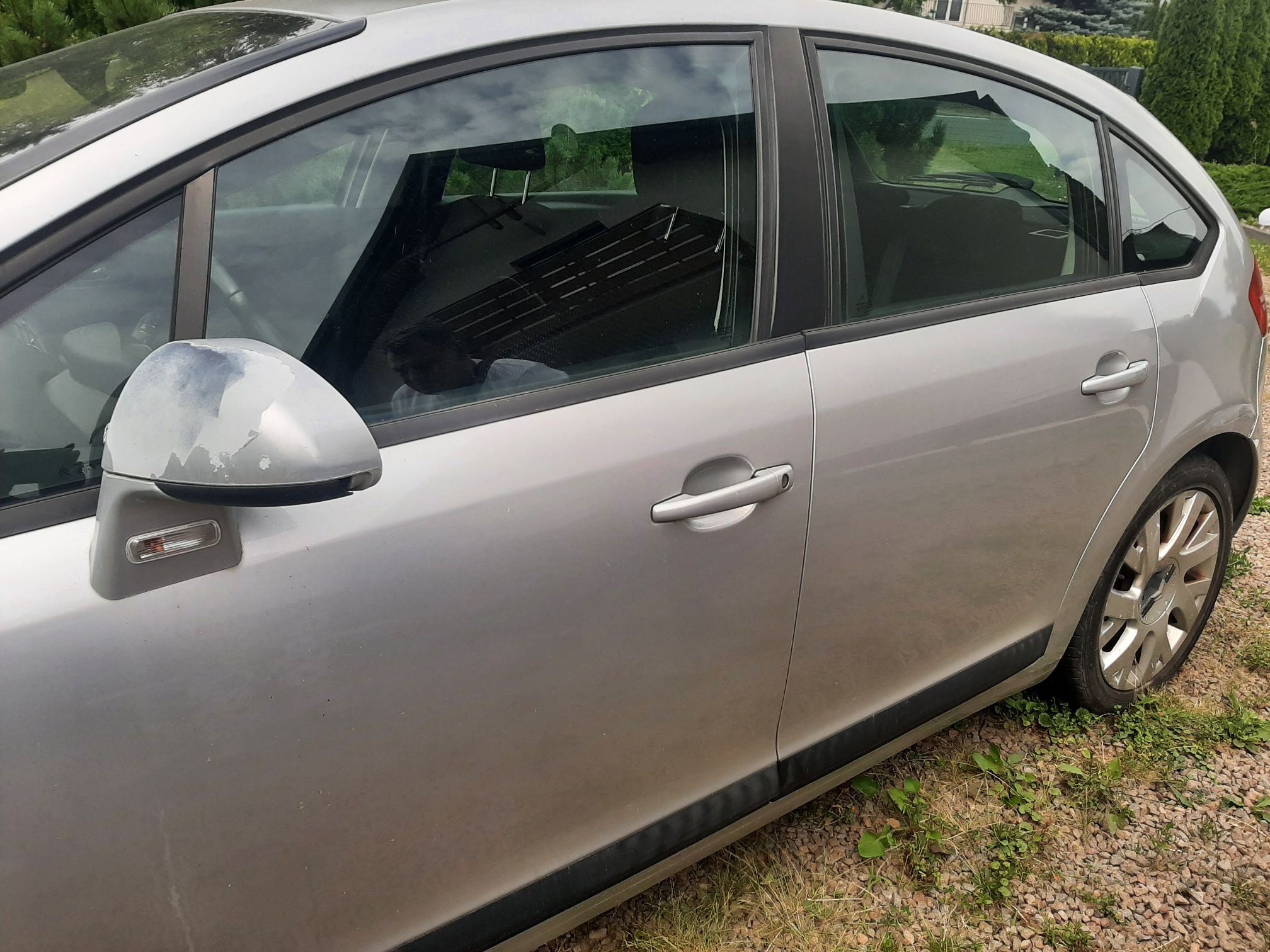 Srebrny Citroen C4 z boku. Widoczne porysowane drzwi pasażera, odrapany lakier na lusterku oraz zarysowany tylny błotnik.