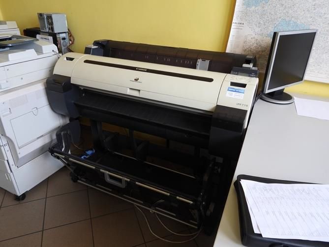 Wielkoformatowy ploter Canon ImagePROGRAF iPF770 stojący na dedykowanej czarnej podstawie z koszem na wydruki.