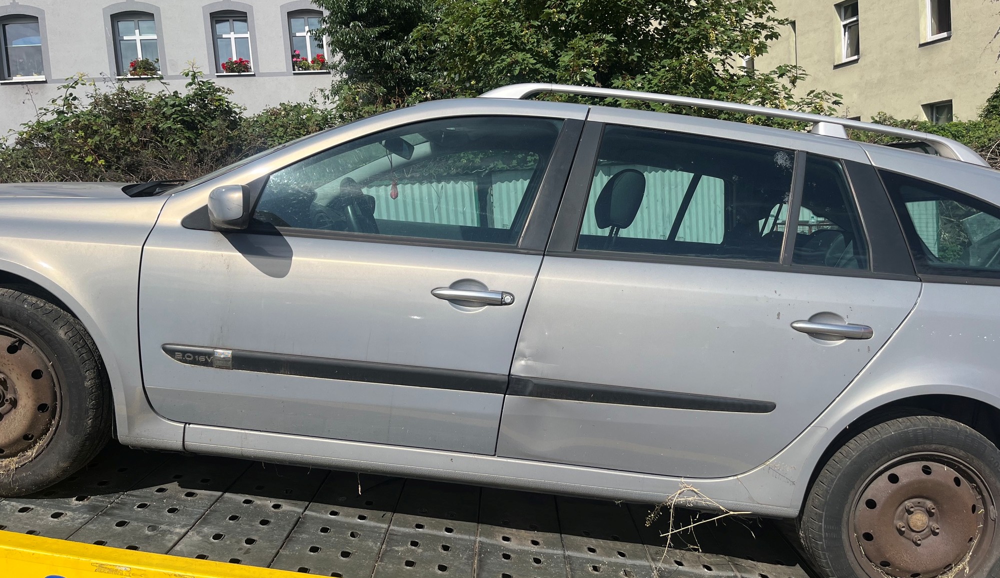 Lewy bok samochodu kombi Renault Laguna z uwidocznionymi na drzwiach wgnieceniami oraz zarysowaniami w dolnej partii.
