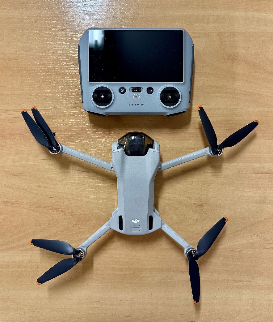 Dron oraz aparatura sterująca w kolorze szarym. Kontroler lotu z ekranem.