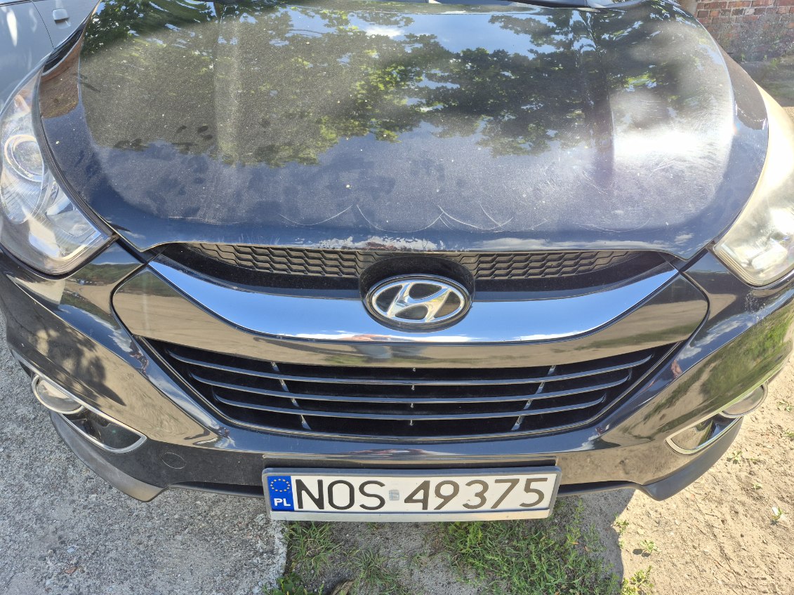 czarny Hyundai ix35, widok z przodu. Maska z wgnieceniami i popękanym lakierem. Widoczne ogniska korozji