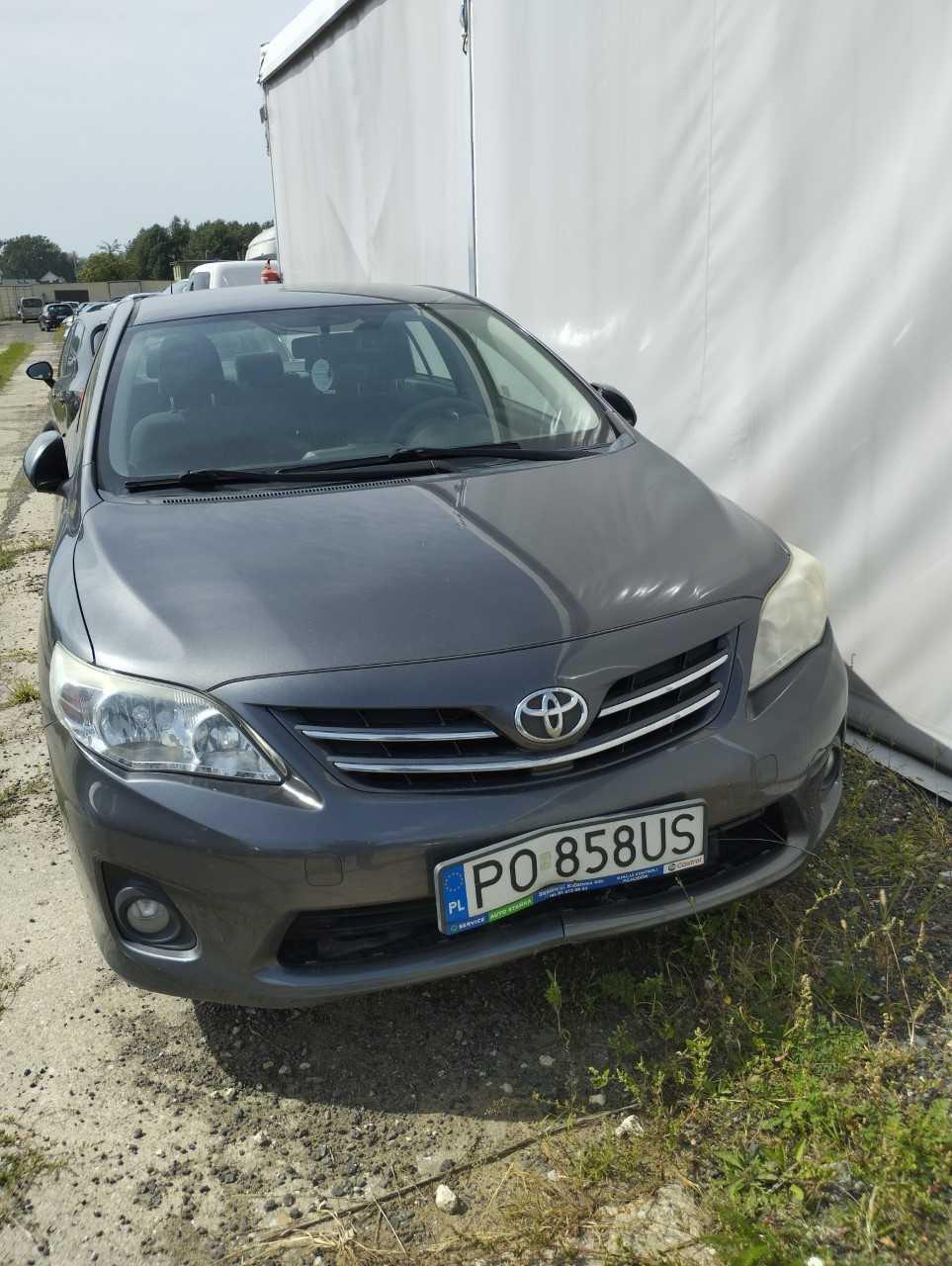 Grafitowy, osobowy samochód marki Toyota Corolla sedan z pękniętym i wgniecionym przednim zderzakiem.