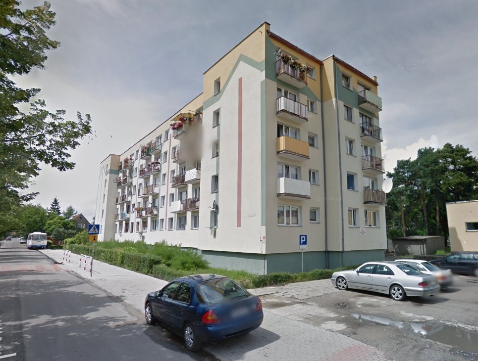 Jasny blok mieszkalny w towarzystwie roślinności oraz parkingu