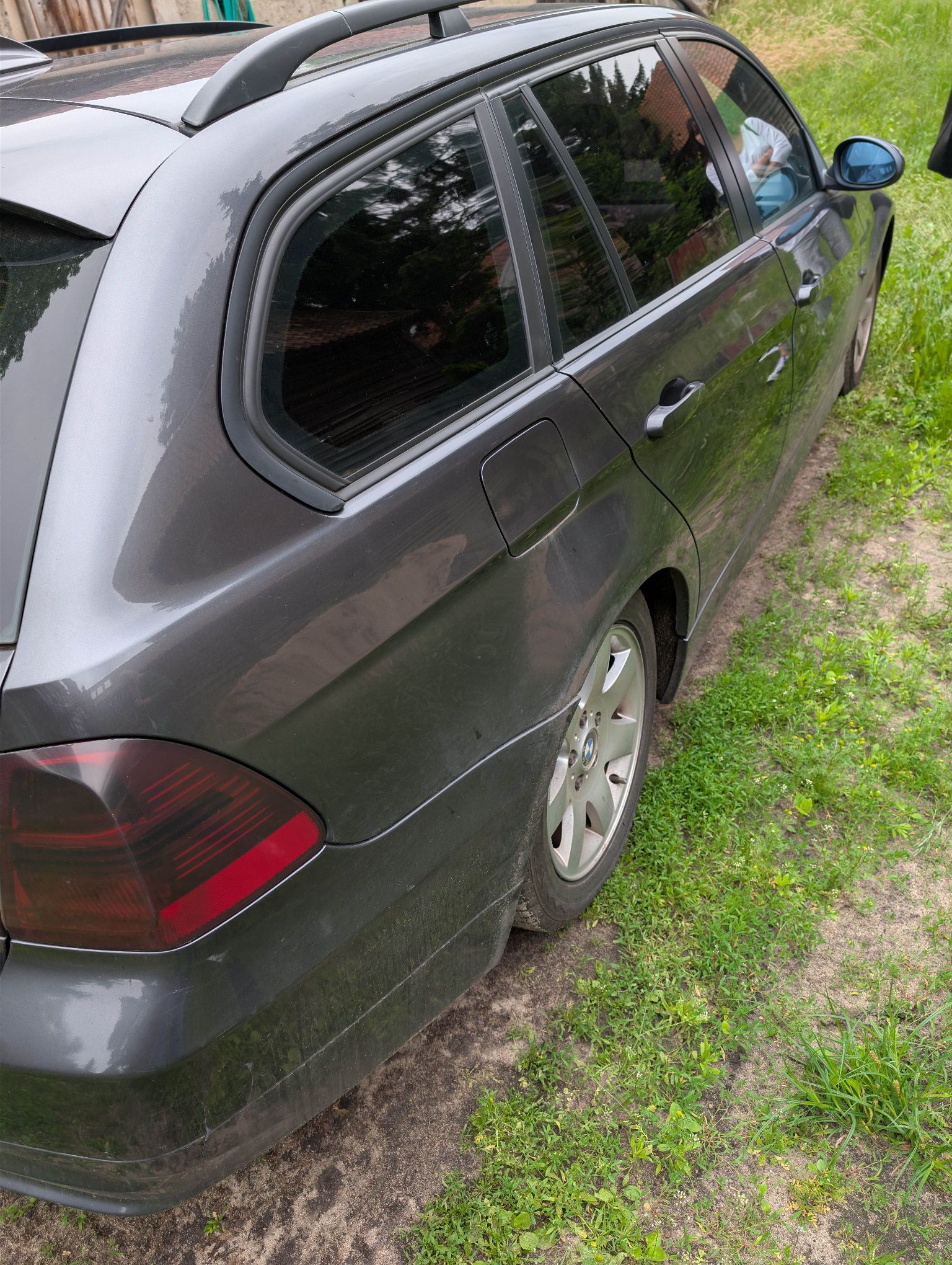 Ciemnoszare kombi BMW sfotografowane z lewej tylnej strony. Przyciemniane tylne szyby, relingi dachowe.