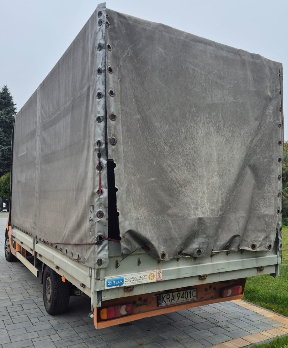 Tył pojazdu Renault Master. Szara plandeka, zderzak pojazdu lekko wgięty.